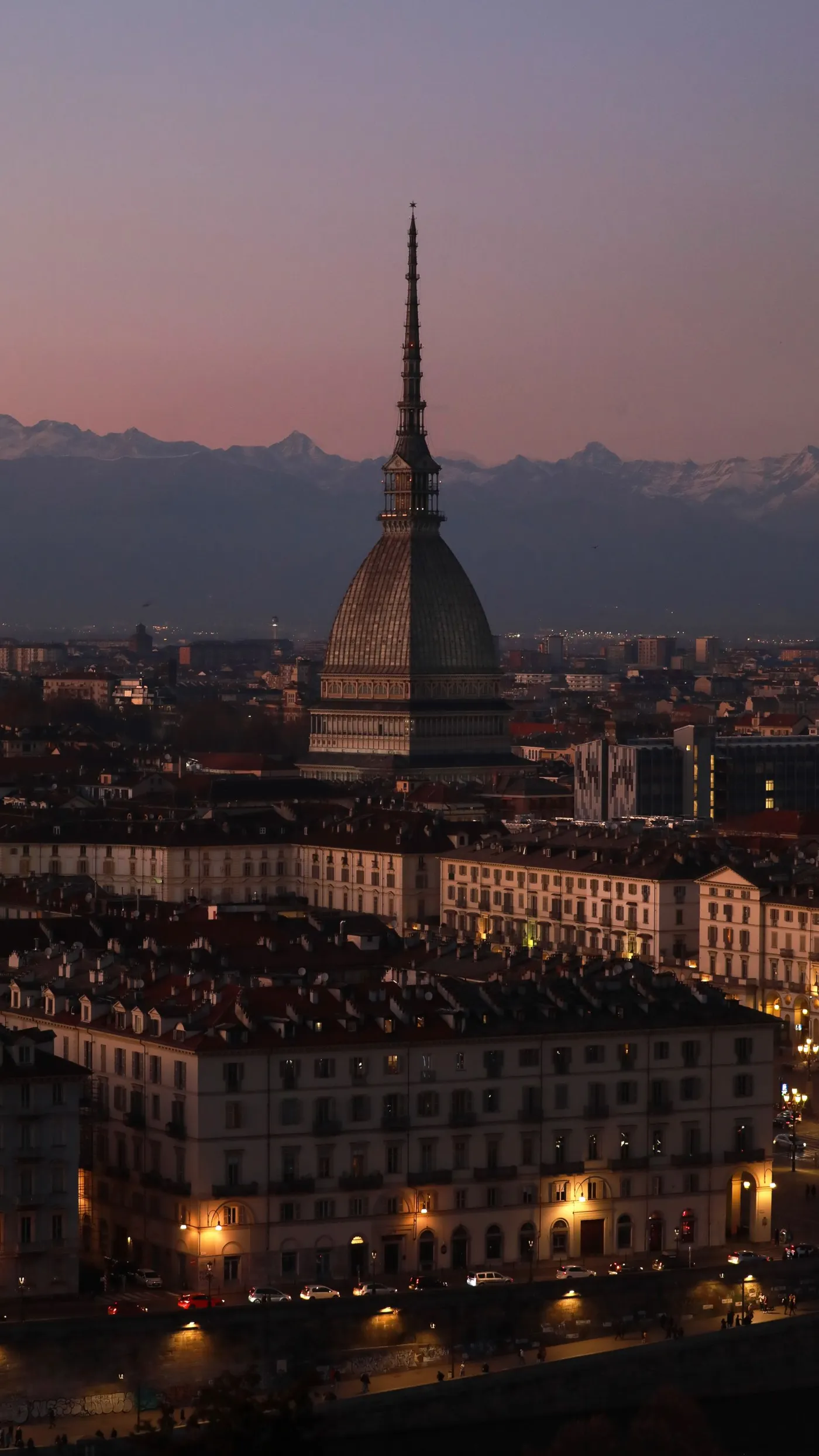 La Mole Antonelliana sopra i tetti di Torino al crepuscolo, con le Alpi sullo sfondo